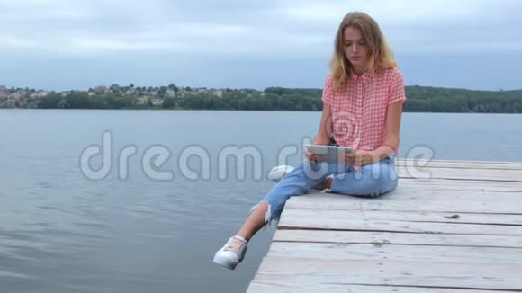 女人在平板电脑前轻敲坐在湖边慢动作视频的预览图