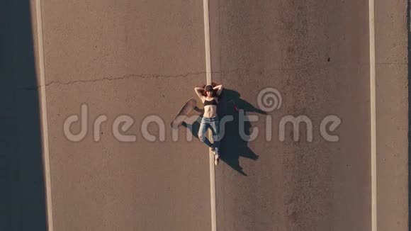 空中飞行女孩嬉皮士用滑板躺在马路上从上面看视频的预览图