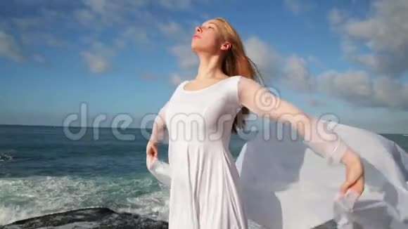 自由概念穿着白色连衣裙和围巾的女人站在岩石上跳舞在飞行移动做体操视频的预览图