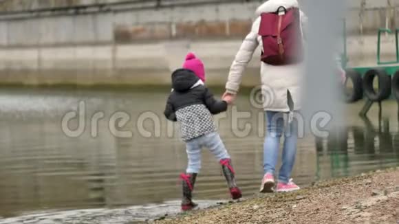 母亲和她的小女儿沿着石滩散步收集贝壳把石头扔进水里视频的预览图