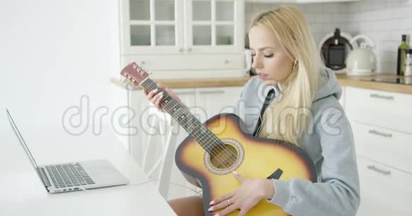 女人一边弹吉他一边用笔记本电脑视频的预览图