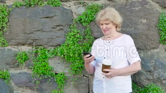 使用智能手机和喝咖啡的老年妇女背景中野石的复古墙视频的预览图