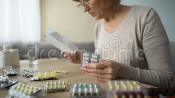 生病的老妇人坐在家里的桌子上读着药说明书药视频的预览图