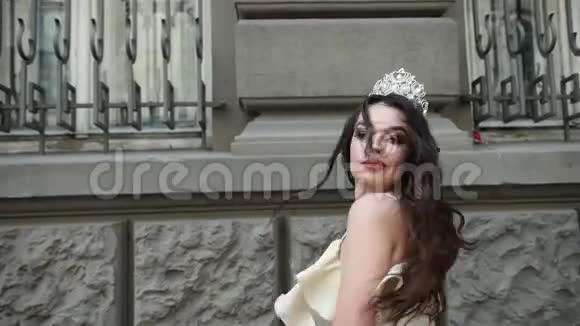 穿着浅色连衣裙戴着皇冠的深色女孩模特在街上拍照视频的预览图
