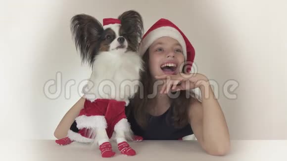 美丽的少女和狗穿着圣诞老人的服装穿着圣诞老人的玩具斯帕尼尔帕皮隆兴高采烈地四处张望视频的预览图