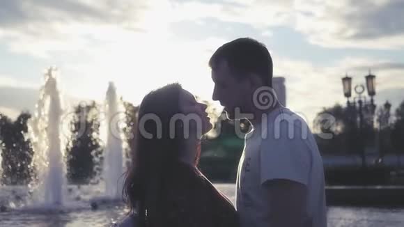 一对相爱的情侣在日落背景下的喷泉附近接吻高清1920x1080慢动作视频的预览图