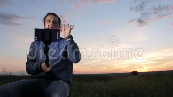 一个年轻人坐在日落时在手机上自拍后面是美丽的天空视频的预览图