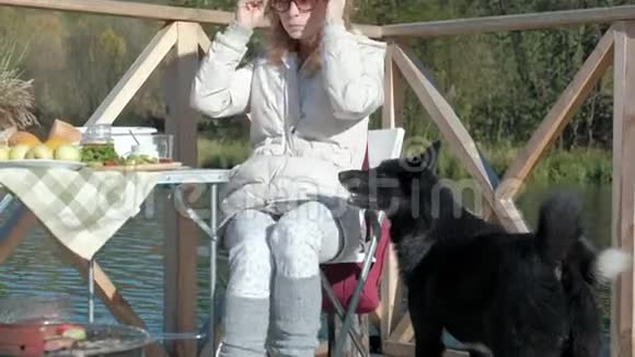 年轻女子穿着暖和的衣服吃着汉堡狗在附近玩耍在河边的木桥上野餐周末视频的预览图