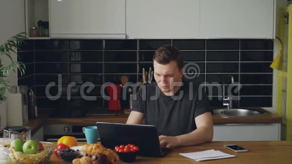 英俊的年轻人在家吃早餐时在厨房里听到好消息读着纸信视频的预览图