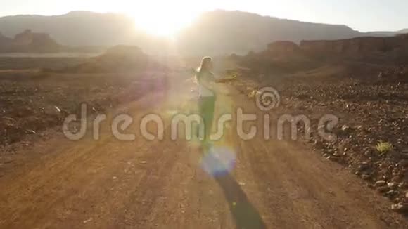 幸福的年轻女子在夕阳下的沙漠道路上行走美丽的太阳耀斑以色列蒂姆纳公园视频的预览图