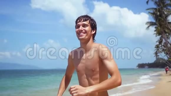 年轻迷人的快乐男人在阳光明媚的日子里缓慢地在海滩上奔跑1920x1080视频的预览图