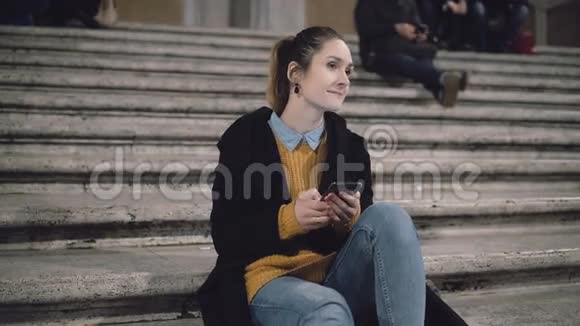学生女孩晚上坐在梯子旁边看着某人微笑着女士使用智能手机浏览互联网视频的预览图