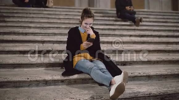 漂亮的年轻学生坐在梯子上使用智能手机女孩与触摸屏技术聊天视频的预览图