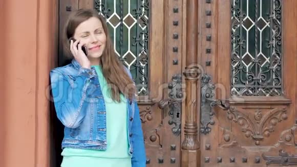 穿着棉袄在智能手机上说话的漂亮女孩背景中的老式建筑视频的预览图