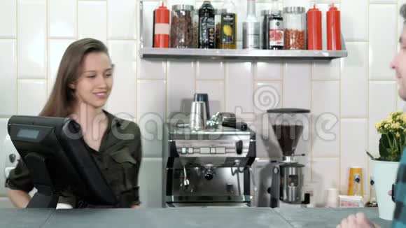 男人在咖啡店里用移动支付男人拿着咖啡用NFC芯片支付无触点的钱在cahbox附近微笑的女人视频的预览图