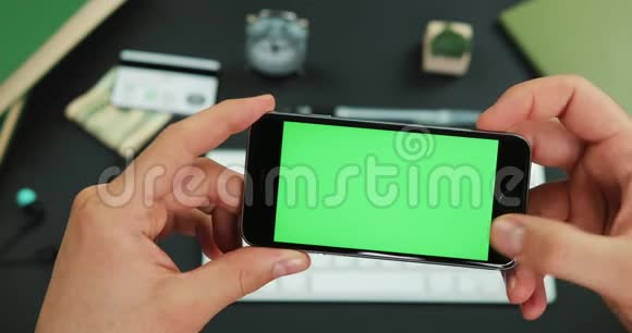 男人拿着绿色屏幕的智能手机在工作桌上滚动一些东西视频的预览图