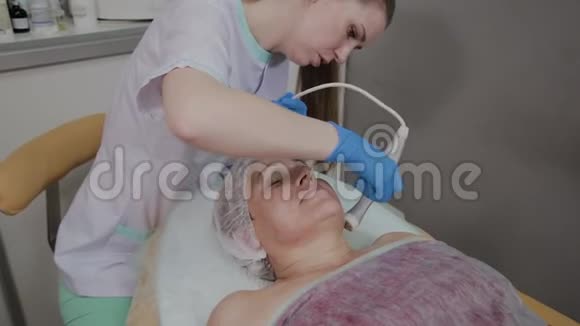 专业美容师在美容办公室为一名携带微电流的老年妇女执行手术视频的预览图
