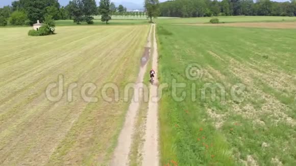 空中男子骑自行车沿着乡间小路穿过耕地和农田阳光明媚的一天环保的交通运输视频的预览图