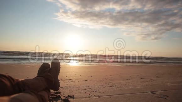 一个人横着两条腿躺在沙滩上穿着靴子享受美丽的柔和日落视频的预览图