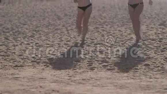 日落时分两个穿着比基尼的年轻漂亮女孩在海滩上奔跑视频的预览图