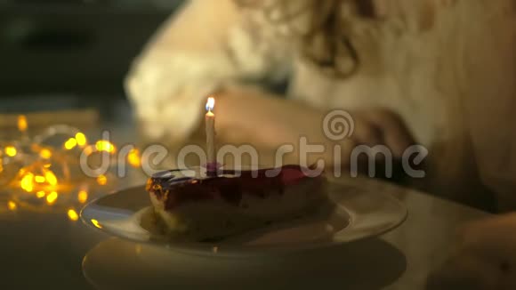 年轻女子拿着盘子和美味的生日蛋糕对着离焦的灯光吹灭了蜡烛视频的预览图