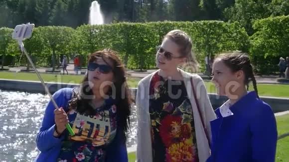 三个女朋友在手机上拍照在湖边的夏季公园里放一根自拍棒慢动作视频的预览图