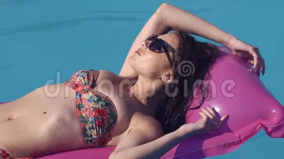 一个年轻漂亮的女孩躺在游泳池里的充气床垫上视频的预览图