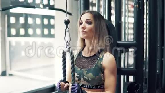 一个年轻的健身女子在健身房用训练机做三头肌运动视频的预览图