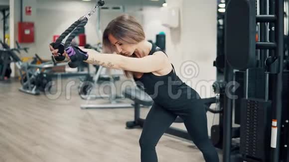 年轻健身女子在健身房使用训练机进行三头肌锻炼的镜头视频的预览图
