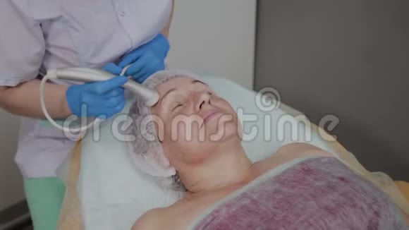 专业美容师在美容办公室为一名携带微电流的老年妇女执行手术视频的预览图