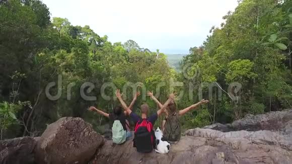 空中三个无忧无虑的徒步旅行者坐在瀑布旁把手从山坡上摔下来高清慢镜头视频的预览图