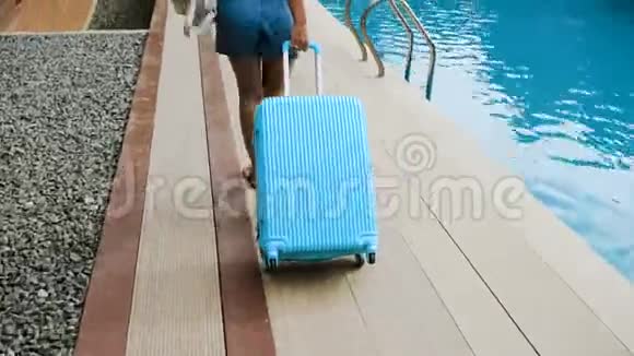 戴着帽子和工作服的金发女孩在一家带着蓝色袋子的热带酒店安顿下来视频的预览图