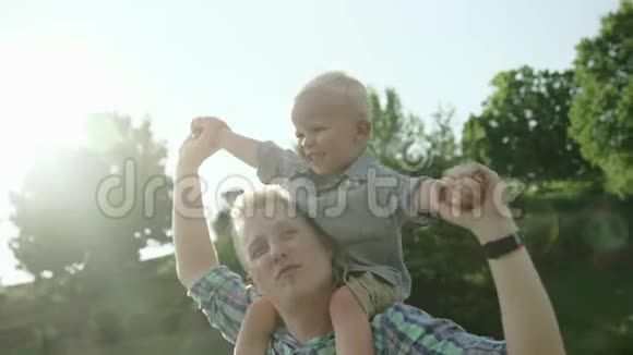 快乐的年轻父亲把儿子背在肩上抬起来小男孩背着背坐着视频的预览图