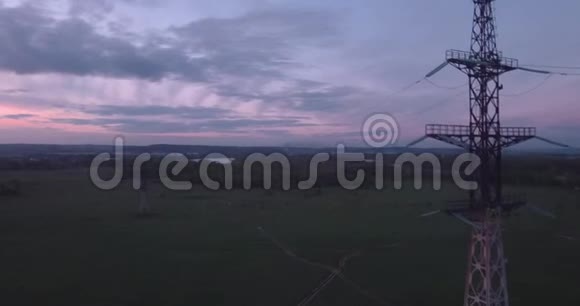 俯视图空中高压塔在田野和小镇的地平线上云彩在夕阳的光芒4K视频的预览图