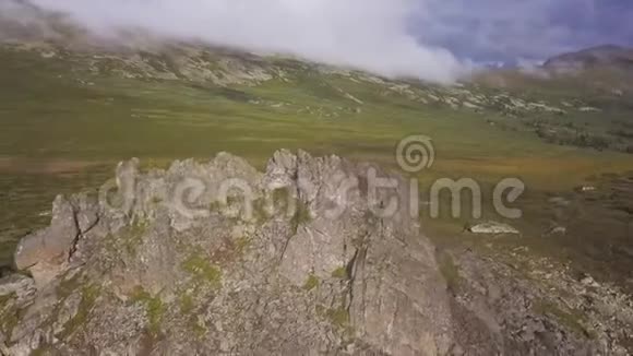 在绿色草地上的鸟瞰有孤独的岩石和多云的天空背景令人惊叹的山景和巨大的岩石在视频的预览图