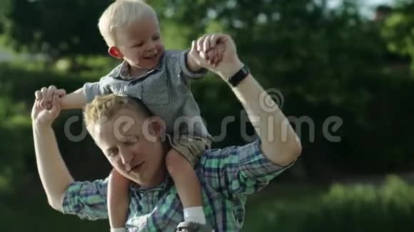 快乐的年轻父亲把儿子背在肩上抬起来小男孩背着背坐着视频的预览图