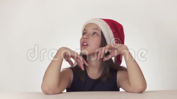 戴着圣诞老人帽子的美丽快乐少女在白色背景的股票片段中表达了一个惊喜视频的预览图