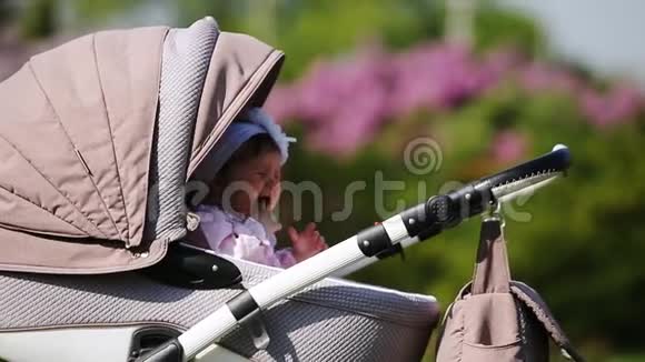 在阳光明媚的日子里哭泣的女婴坐在公园里的婴儿车厢里视频的预览图