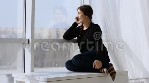 年轻快乐的女人在打电话阳光明媚的一天坐在窗边视频的预览图
