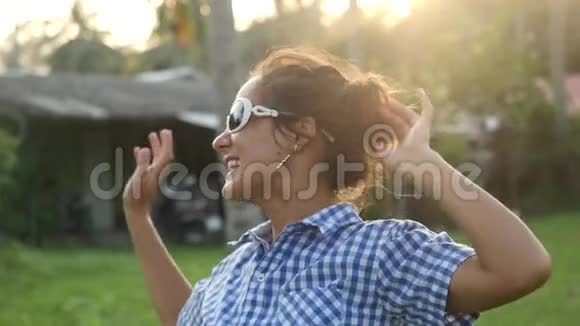 快乐时尚的年轻女士戴着太阳镜在太阳下在热带棕榈树之间跳舞在日落时享受他的假期视频的预览图