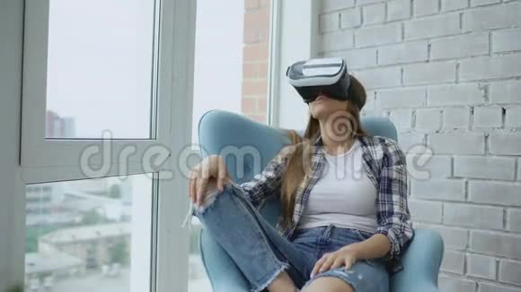 年轻女性使用虚拟现实耳机坐在阳台上的椅子上有VR体验视频的预览图