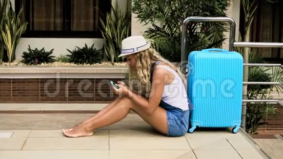 戴着帽子的金发女孩穿着蓝色包的工作服住在一家带游泳池的热带酒店里4K视频的预览图