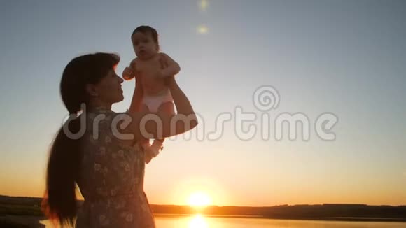 妈妈在日落时抱着孩子在太阳的怀抱里慢动作视频的预览图