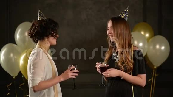 两个女朋友拿着香槟和葡萄酒在黑色背景下用空气气球互相交谈视频的预览图