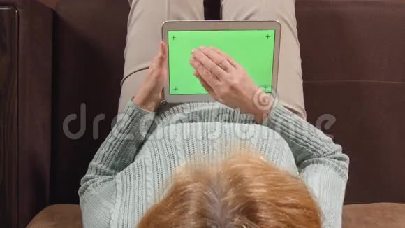 顶部视图老年妇女沙发上有平板电脑绿色屏幕特写视频的预览图