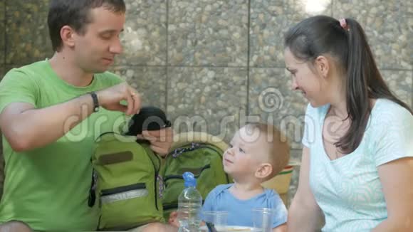一个带着孩子的年轻家庭正在测量婴儿的太阳镜妈妈爸爸和宝宝正坐在公园咖啡馆里视频的预览图