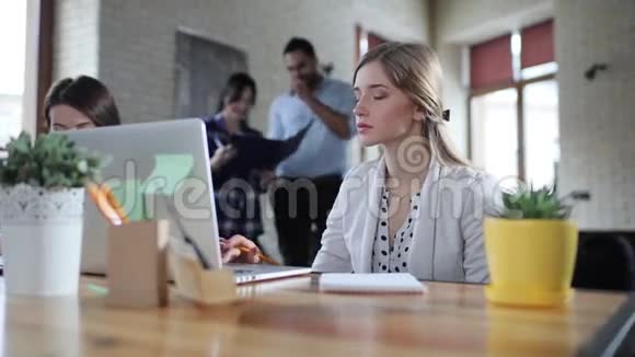 商务女性坐在办公室手提电脑在笔记本上写新想法其他工人可以看到视频的预览图