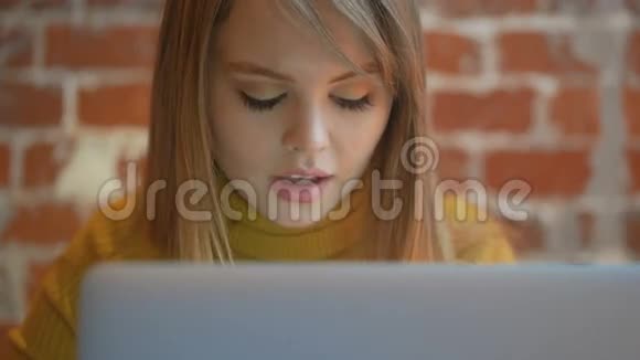年轻可爱的女孩坐在笔记本电脑旁边看着屏幕小工具使用的概念视频的预览图