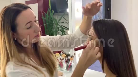 美容院年轻漂亮的女孩模特坐在椅子上化妆师让化妆女孩视频的预览图