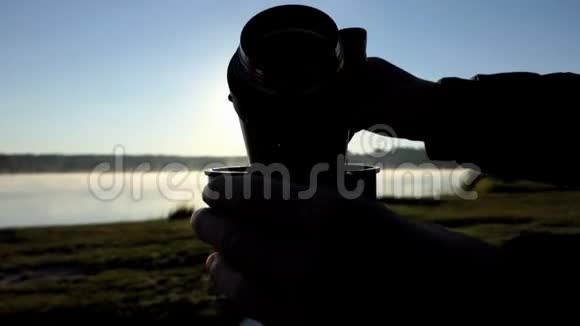 日落时分绿茶倒在湖岸的烧瓶杯里视频的预览图